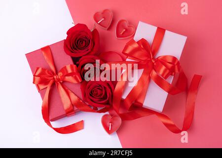 Grußkarte zum Valentinstag, Muttertag und Geburtstag. Rote Rosen, Geschenkschachteln mit einer Schleife aus rotem Satinband auf pinkfarbenem Hintergrund. Draufsicht, flach Stockfoto