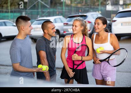 Zwei Tennisspielerpaare diskutieren gerne das letzte Spiel auf dem Parkplatz Stockfoto