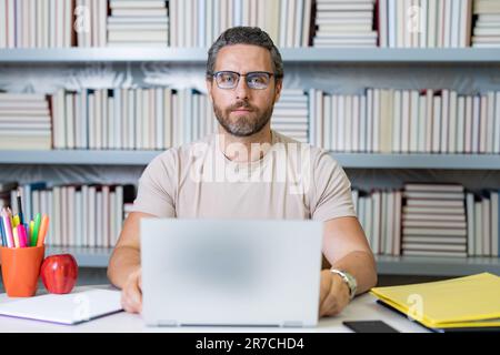 Porträt eines Lehrers mit Laptop im Klassenzimmer. Hübscher Lehrer im Klassenzimmer. Lehrertag. Guter Lehrer. Nachhilfe im Klassenzimmer. Mann, der Lehrer benutzt Stockfoto