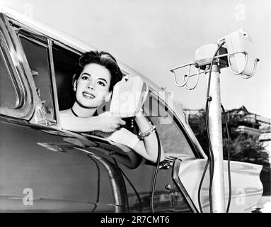 Hollywood, Kalifornien: 1957. Natalie Wood zeigt die neuen Drive-in-Movie-Lautsprecher, während sie sich aus dem Autofenster lehnt. Stockfoto