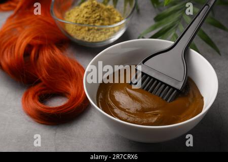 Schüssel mit Henna-Creme, Bürste und rotem Strang auf hellgrauem Tisch, Nahaufnahme. Natürliche Haarfarbe Stockfoto