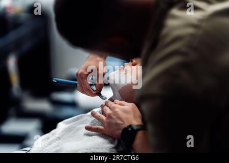 Ein Friseur rasiert einen Mann mit einem gefährlichen Rasierer. Stockfoto