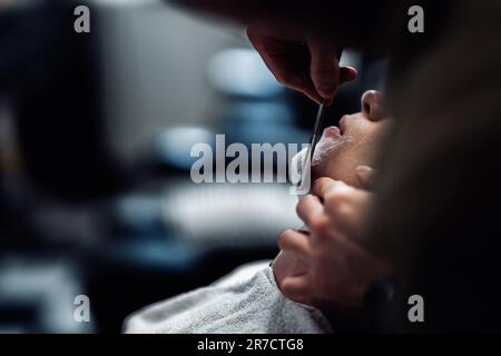 Ein Friseur rasiert einen Mann mit einem gefährlichen Rasierer. Stockfoto