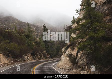 Eine lange, kurvenreiche Straße, die sich durch die nebelbedeckten Berge schlängelt Stockfoto