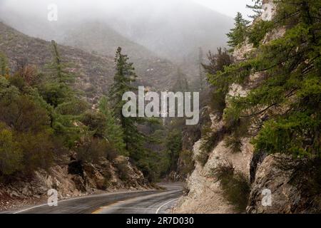 Eine lange, kurvenreiche Straße, die sich durch die nebelbedeckten Berge schlängelt Stockfoto
