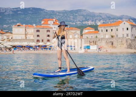Junge Frauen, die Spaß haben, paddeln im blauen Meer in Montenegro. Vor dem Hintergrund der Altstadt von Budva. WAS GEHT AB Stockfoto