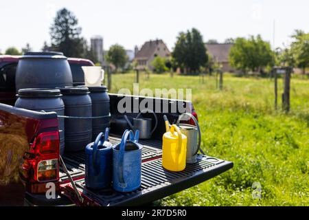 Staufen Im Breisgau, Deutschland. 14. Juni 2023. Gießkannen und Wasserfässer stehen auf dem Ladebereich des Obstbauers M. Geng (nicht im Bild), während junge Obstbäume im Hintergrund zu sehen sind. Die Gießdosen sind für die Bewässerung junger Bäume gewöhnt. Die anhaltende Dürre in Südbaden bereitet der Natur Probleme, und viele Landwirte sind besorgt über die Ernteerträge. Kredit: Philipp von Ditfurth/dpa/Alamy Live News Stockfoto