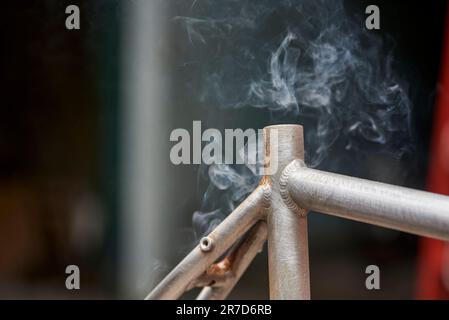 Rauchen von Metall, manuelle Renovierungsarbeiten an Fahrrädern, Lackentfernung durch Brennerfeuer, um die Farbe eines Fahrradrahmens zu ändern. Nahaufnahme, keine Menschen. Stockfoto