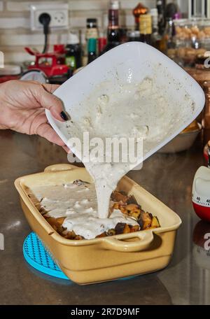 Der Koch gießt Soße über gewürfelte Auberginen zum Backen im Ofen. Stockfoto