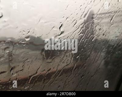 Ein Fenster, bedeckt mit Wassertropfen eines Zuges, der sich durch eine Landschaft bewegt, in der es regnet Stockfoto