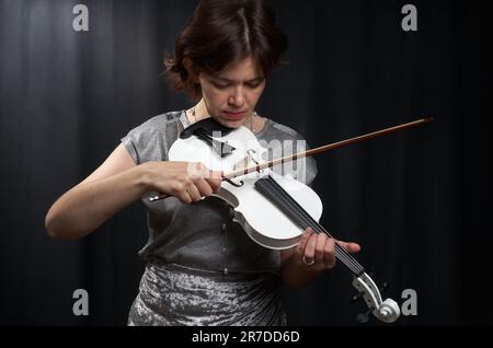 Ein halblanges Porträt einer Frau, die Geige spielt, auf schwarzem Hintergrund Stockfoto