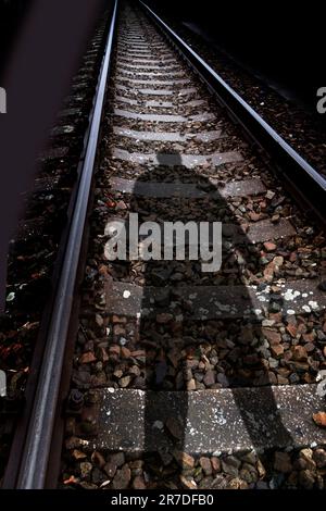 Der Schatten eines mysteriösen Mannes, der über einer Eisenbahnstrecke steht Stockfoto