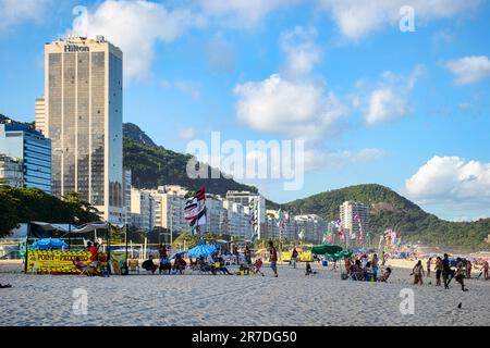 Rio de Janeiro, Brasilien - 25. Mai 2023: An einem sonnigen Tag bevölkern Gruppen den Strand von Copacabana. Ein Stadtbild mit hohen Gebäuden, eines mit dem Namen Hilton, dez. Stockfoto