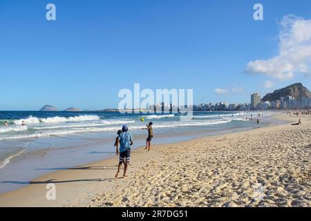 Rio de Janeiro, Brasilien - 25. Mai 2023: Die Jungen spielen am Copacabana Beach ein Spiel, umgeben von anderen Strandgängern, die schwimmen, sitzen und stehen. Stockfoto