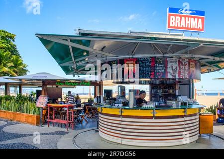 Rio de Janeiro, Brasilien - 25. Mai 2023: Ein Mann sitzt in einer Bar am Copacabana-Strand mit einem Brahma-Schild auf dem Dach. Andere Leute haben Stühle und Stühle Stockfoto