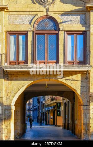 Oviedo, Spanien - 12. Februar 2023: Eine Architektur mit Glasfenstern und einem Erdgeschossgang. Der Korridor enthüllt entfernte Gebäude und Menschen Stockfoto