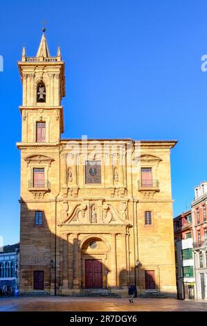 Oviedo, Spanien - 12. Februar 2023: Ein altes Gebäude mit Glockenturm und Skulptur an der Fassade. Ein Mann geht in der Nähe und fängt die Essenz der Kunst und ein Stockfoto