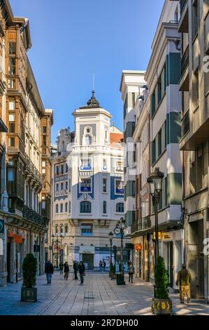 Oviedo, Spanien - 12. Februar 2023: Menschen, die auf einer Stadtstraße mit Bürgersteigen, umgeben von hohen Gebäuden mit Balkonen, spazieren gehen. Die Strukturen werden dargestellt Stockfoto