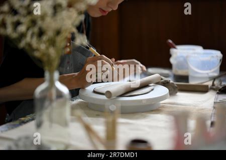 Nahaufnahme eines professionellen männlichen Töpferkünstlers, der ein Bildhauer-Werkzeug hält, Muster auf rohem Ton macht und in seinem Kreativstudio arbeitet. Stockfoto