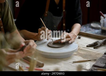 Nahaufnahme eines professionellen männlichen Töpferkünstlers, der einen Stock hält, Muster auf rohem Ton macht, in seinem Kreativstudio arbeitet. Stockfoto