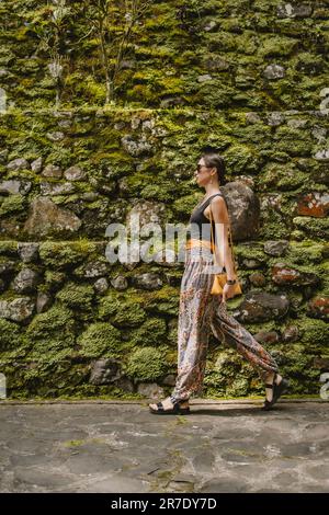 Ein wandelndes junges, stilvolles Mädchen mit Tempelwand-Hintergrund. Puru Gunung Kawi antike Architektur, weibliche Touristen in einem felsigen Tempel Stockfoto