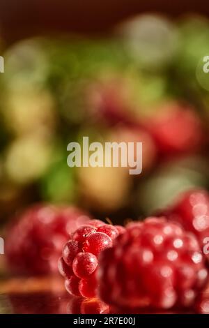 Verschwommener Hintergrund rote Himbeeren und grüne Blätter. Abstrakter, mehrfarbiger heller Hintergrund mit Himbeeren. Stockfoto