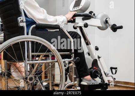 Eine nicht erkennbare ältere Frau macht Pedalübungen vom Rollstuhl im Krankenhaus. Hochwertiges Foto. Stockfoto