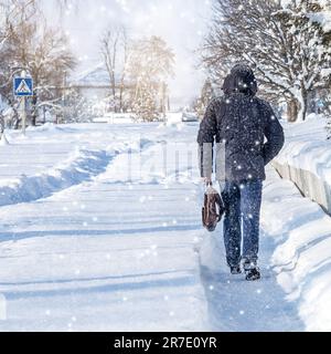 Ein Mann geht im Winter die Straße entlang. Ein Mann geht während der Schneesaison auf dem Bürgersteig entlang. Ein Mann geht im Winter zur Arbeit. Stockfoto