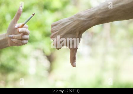 Raucherentwöhnungstag. Die Hand des Mannes sagt nein, eine Zigarette. Daumen nach unten. Weibliche Hand hält eine Zigarette. Rauchen stoppen und Gesundheitskonzept Stockfoto