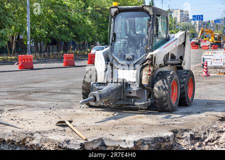 Ein kleines und manövrierbares Baufahrzeug mit angebrachtem Presslufthammer steht auf einem Bau- und Reparaturbereich einer Stadtstraße. Stockfoto