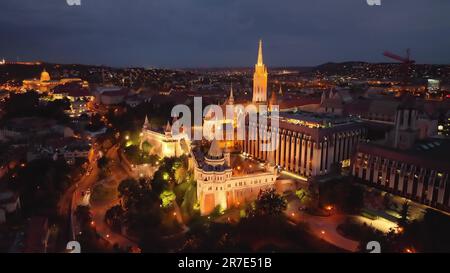 4K Drohne, die in der beleuchteten Fischerbastei von der Matthiaskirche mit Uhrturm fliegt. Budapest, Ungarn Stockfoto