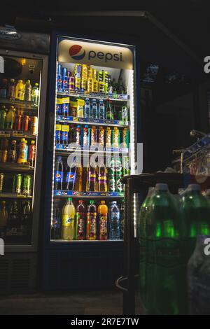 Ein Laden mit einem Kühlschrank gefüllt mit kalten Softdrinks, Getränken, Flaschen, Dosen und Lampen an der Maschine macht es zu einem Kinoerlebnis Stockfoto