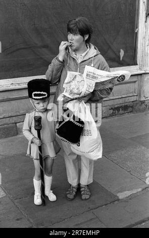 Ein junges Mädchen im Drum-Majorettes-Kostüm mit ihrer Mutter, die ein Fish-and-Chip-Essen zum Mitnehmen aus einer Zeitung isst. Byker Newcastle Upon Tyne, Tyne und Wear, Nordengland um 1973. 1970S GB HOMER SYKES Stockfoto