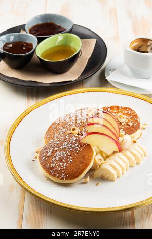Pfannkuchen mit Obst und eine Tasse Kaffee auf weißem Holzhintergrund. Leckeres Frühstück. Stockfoto
