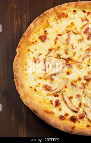 Pizza mit Schweinegurken, Tomatensauce, gemischter Käseauswahl und Zwiebeln auf Holzhintergrund. Stockfoto