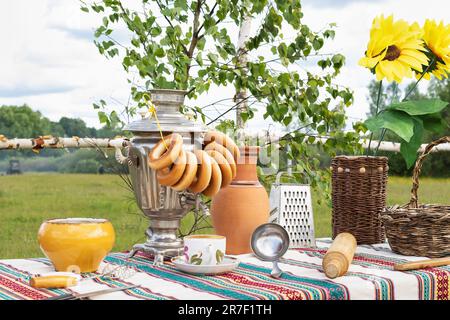 Ein alter russischer rustikaler Tisch mit Samovar, Bagels und anderen Küchenutensilien draußen im Garten Stockfoto