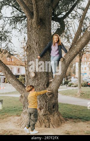 Zwei lustige Kinder spielen draußen im Spring Park, klettern auf den Baum, Bruder und Schwester haben Spaß zusammen Stockfoto