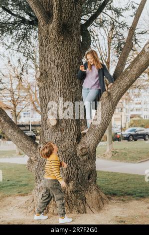 Zwei lustige Kinder spielen draußen im Spring Park, klettern auf den Baum, Bruder und Schwester haben Spaß zusammen Stockfoto