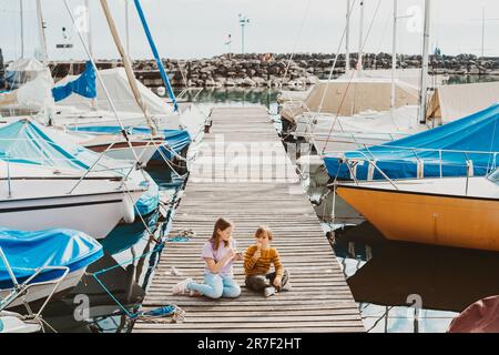 Junge Kinder essen Eis im Freien und ruhen sich auf einem Pier am See aus Stockfoto