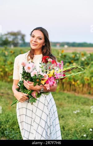 Außenporträt einer schönen und glücklichen Frau, die einen Strauß bunter Blumen in der Natur hält Stockfoto