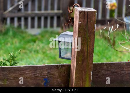 Eine gereifte Laterne auf einem Holzpfahl eines rustikalen Gartenzauns, umgeben von üppigem Grün Stockfoto