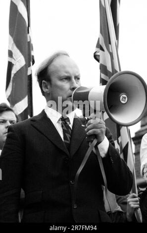 John Tyndall, Anführer der Front National, Lewisham, London.1977 die Polizei beschützt Mitglieder der Front National während der so genannten Schlacht von Lewisham, die am 13. August stattfand. 500 Mitglieder der Nationalen Front marschierten vom Neuen Kreuz nach Lewisham, verschiedene Gegendemonstrationen von etwa 4.000 Personen führten zu gewaltsamen Auseinandersetzungen zwischen den beiden Gruppen sowie zwischen den Anti-NF-Demonstranten und der Polizei. GROSSBRITANNIEN 1970ER JAHRE HOMER SYKES Stockfoto