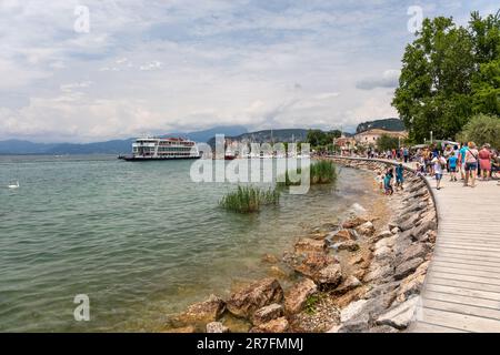 Tonal Ferry Ankunft in Bardolino, während Touristen entlang der Promenade, Bardolino, Gardasee, Italien, Europa spazieren Stockfoto