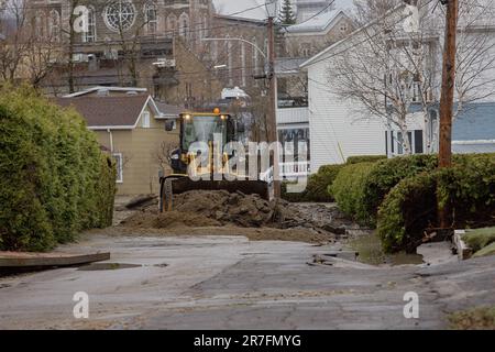 Ein Bagger entfernt den Boden und Schlamm, der sich nach dem Überlauf des Gouffre in Baie St-Paul am 2. Mai 2023 auf der Menard Street ablagerte. Starke Regenfälle in der Region Charlevoix führten zu Überflüssen in Baie St-Paul und den umliegenden Gebieten, was zu einer Überschwemmung und erheblichen Schäden an Wohnhäusern, Unternehmen und Infrastruktur führte. Stockfoto