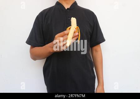 Der Mann im schwarzen Hemd steht und hält eine Banane Stockfoto