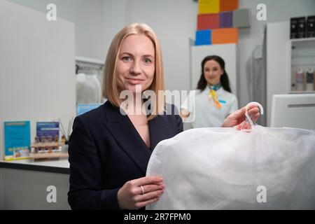 Eine lächelnde Kundin, die einen Kleiderbügel mit sauberer Kleidung hält Stockfoto