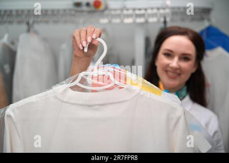 Frau als Chefin der Wäscherei hält Kleiderbügel mit weißem T-Shirt Stockfoto