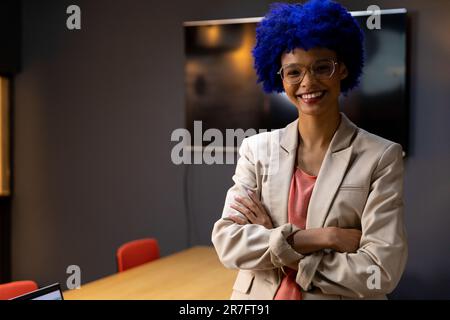 Porträt einer glücklichen, birassischen, lässigen Geschäftsfrau mit blauem Afro, das im Amt lächelt Stockfoto