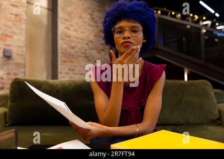 Rücksichtsvolle, birassistische, legere Geschäftsfrau mit blauem Afro, die während eines Videoanrufs im Büro zuhört Stockfoto