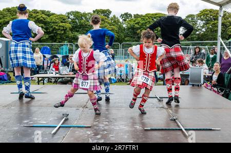 Junge Mädchen, die bei einem Highland-Schwert-Tanz in traditionellen schottischen Kleidern Kilts, Highland Games, North Berwick, Schottland, Großbritannien, gegeneinander antreten Stockfoto